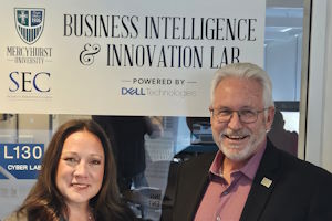 image of Elizabeth Brisson and Bob Hayes of the Security Executive Council in front of the new Business Intelligence and Innovation Lab at Mercyhurst University